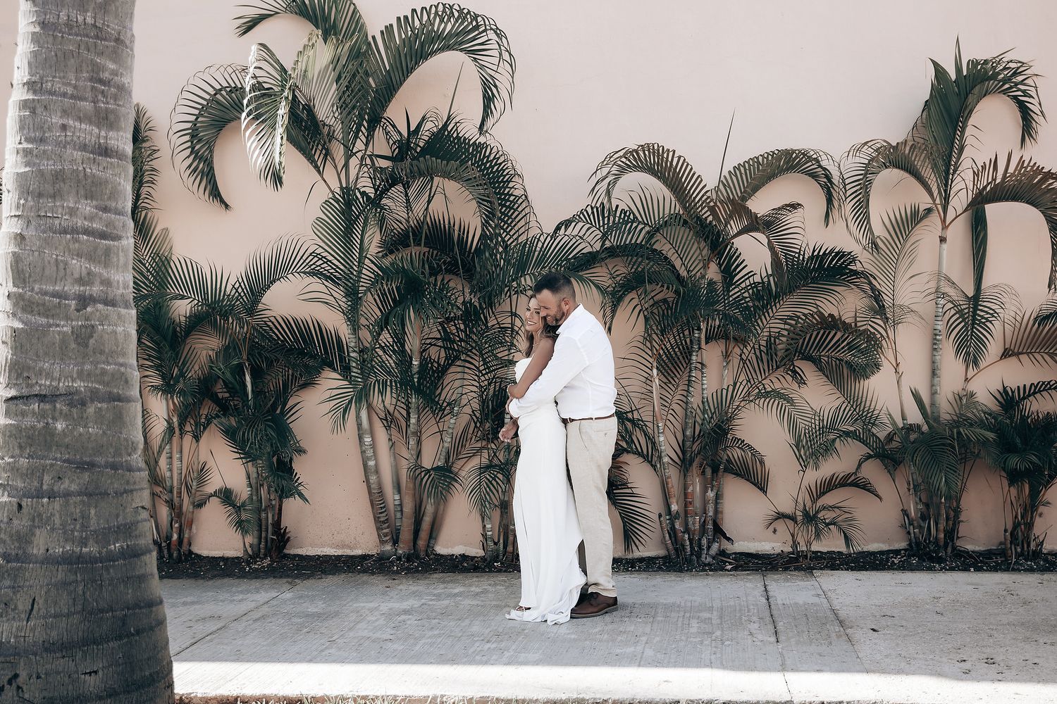 A person wearing a white suit standing in front of a colorful mural with palm trees.