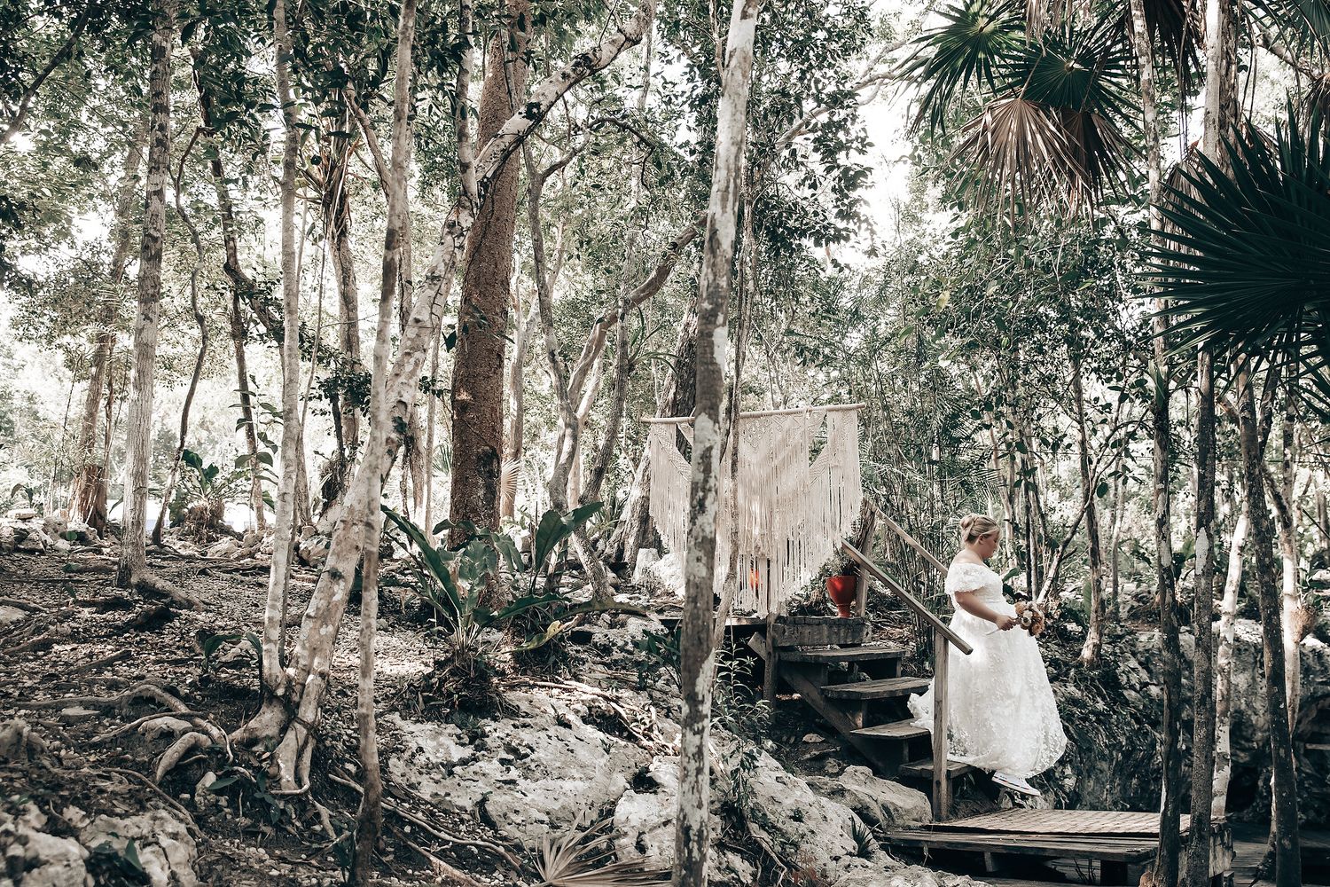 A person dressed in traditional indigenous attire standing on a wooden platform in a forested setting.