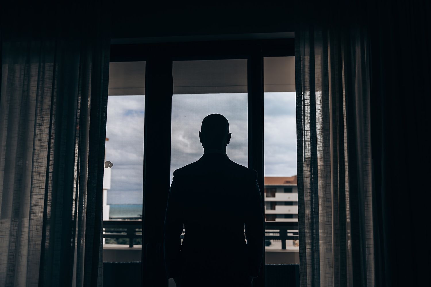 A silhouette of a person standing in a window frame, with a view of the outside visible.