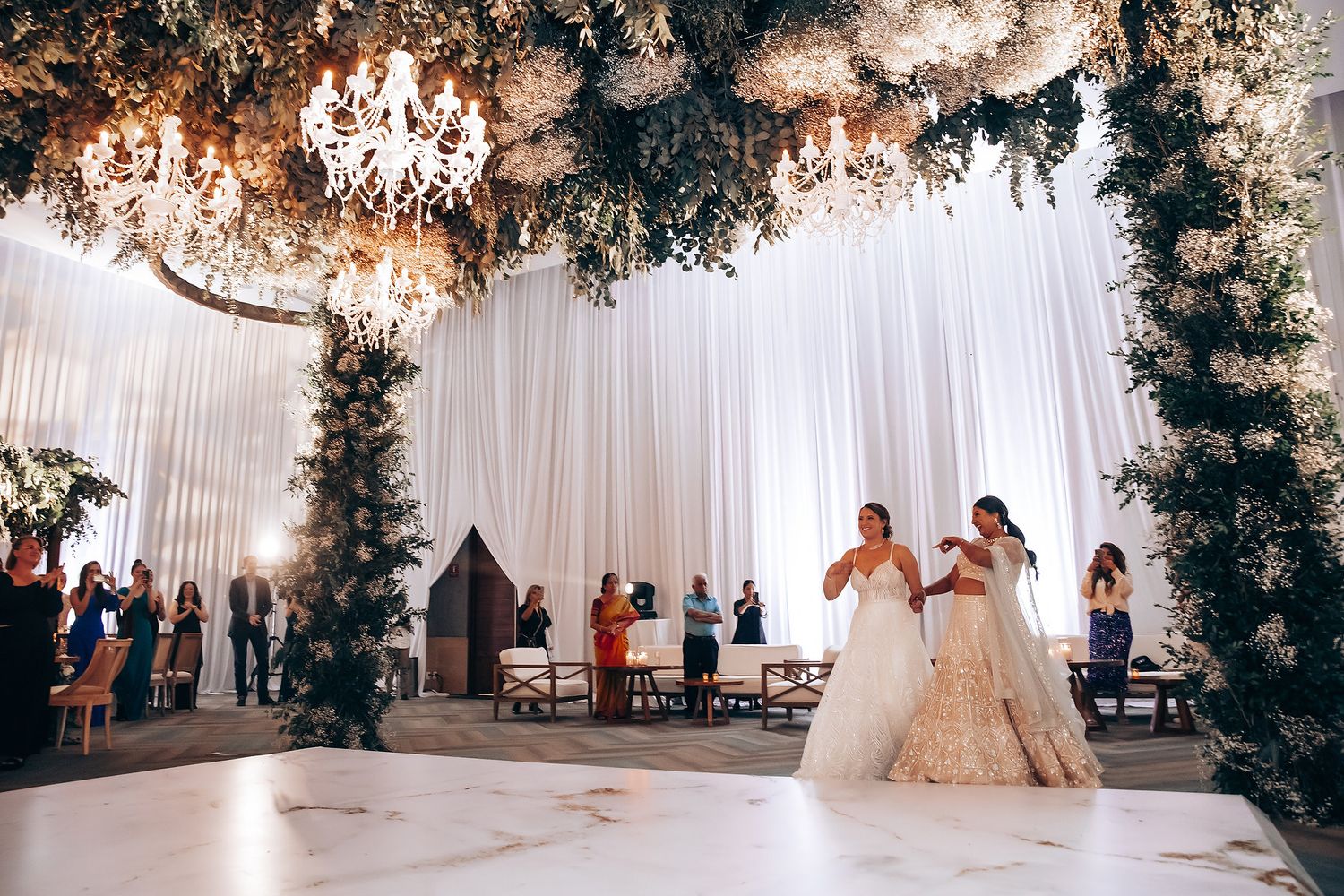 Elegant indoor wedding venue decorated with floral archways, chandeliers, and white drapery.