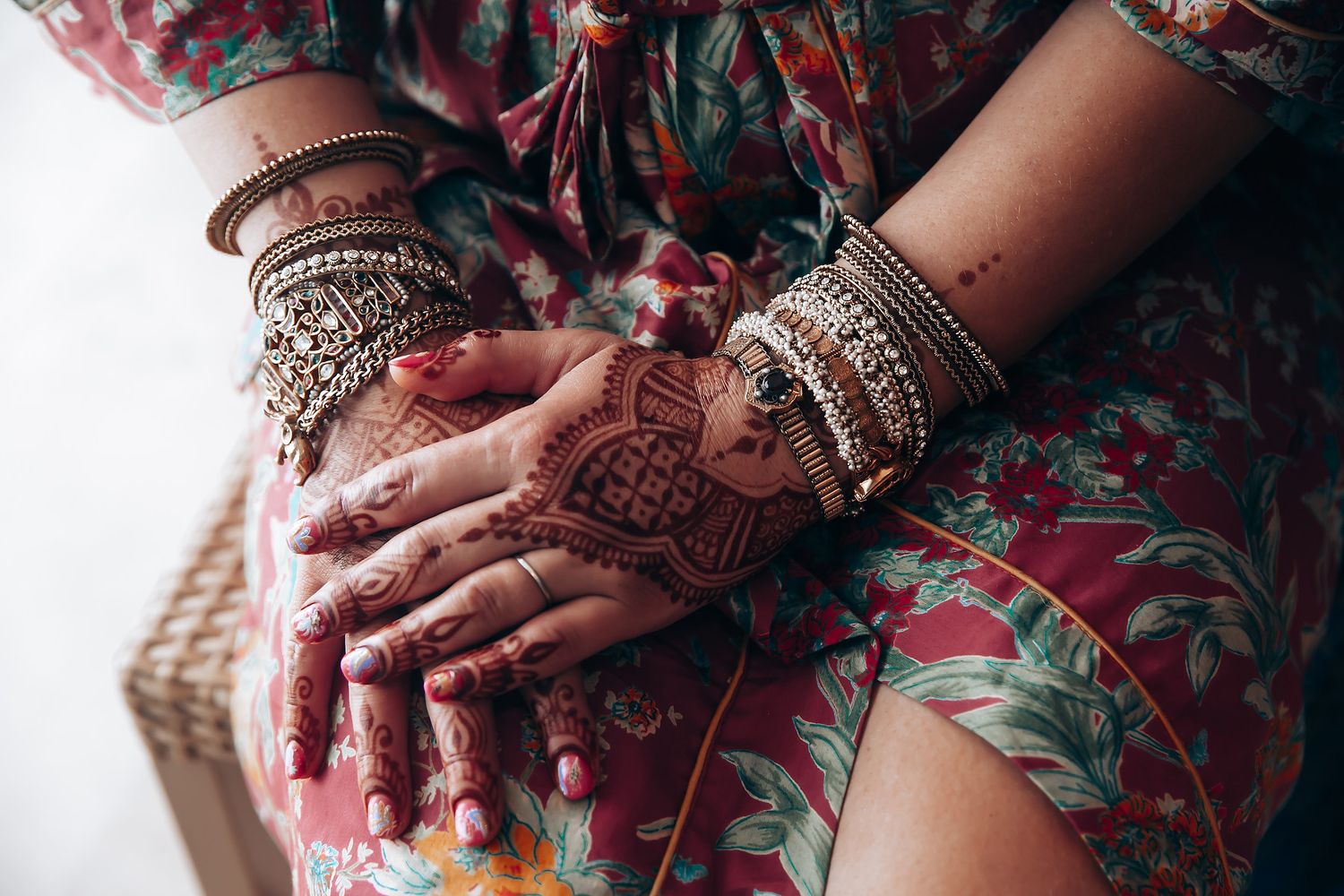 Hands adorned with intricate henna designs and traditional Indian bangles rest on a floral patterned dress.