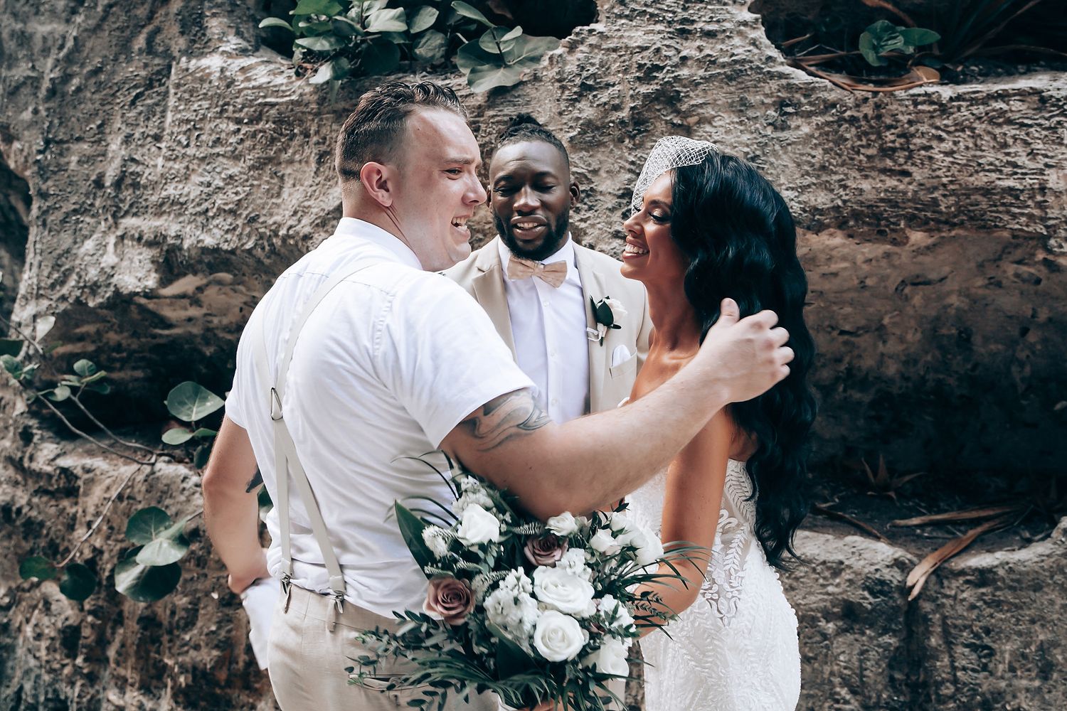 Newlyweds sharing romantic moments against stone wall backdrop.