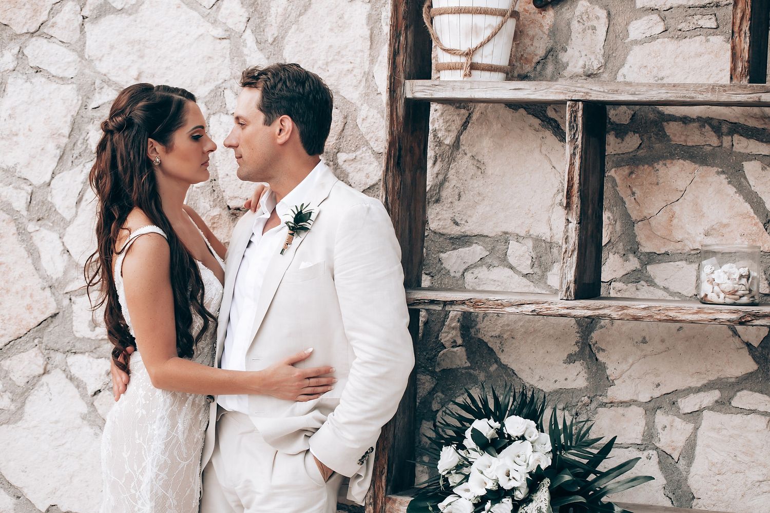 Romantic wedding portrait against rustic stone wall with built-in shelving.