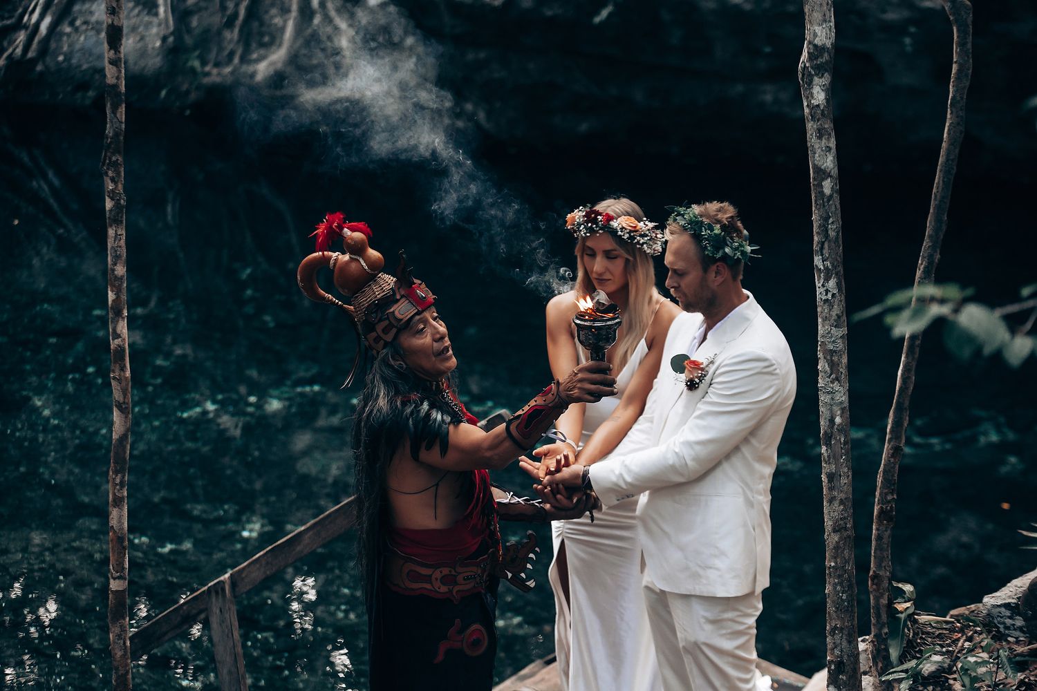 An intimate forest wedding photoshoot with couples embracing among trees in dark, atmospheric lighting.