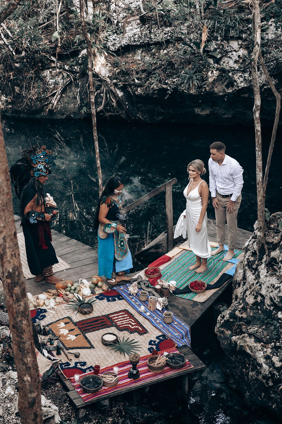 Wedding ceremony space decorated with colorful rugs and cushions in natural cave setting.