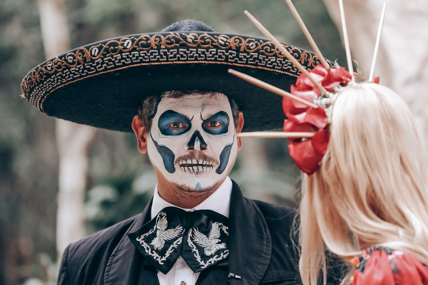 A person wearing Dia de los Muertos makeup and a traditional Mexican sombrero in a forest setting.