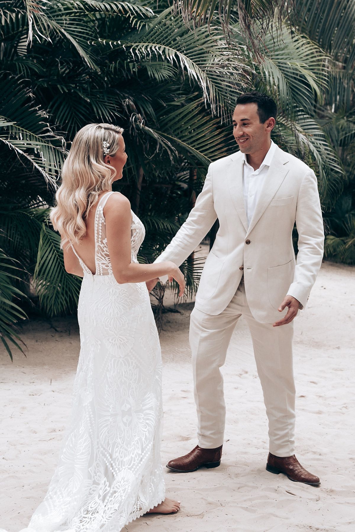 Wedding couple sharing playful moment on tropical beach surrounded by palm trees.