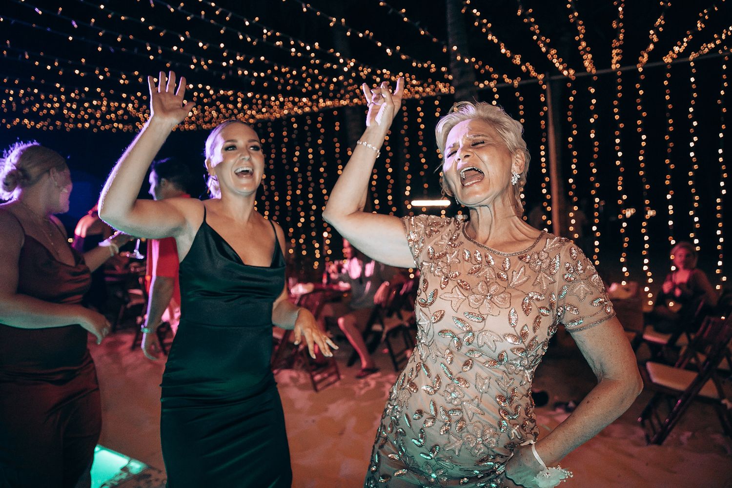 Wedding reception dance floor illuminated with string lights as guests celebrate.