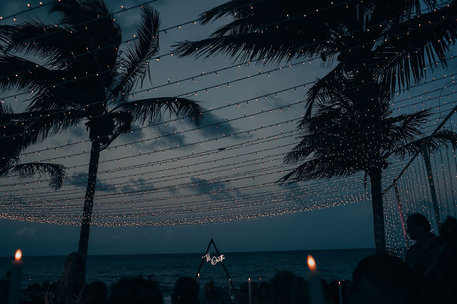 Palm trees silhouetted against twilight sky with string lights creating romantic ambiance.