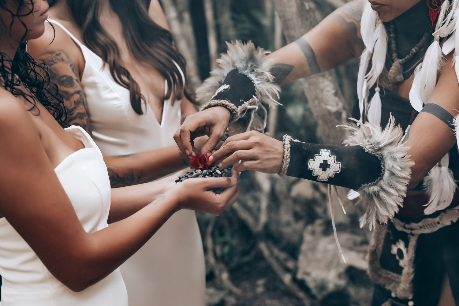 Two people in white dresses hold hands while surrounded by lush tropical vegetation.