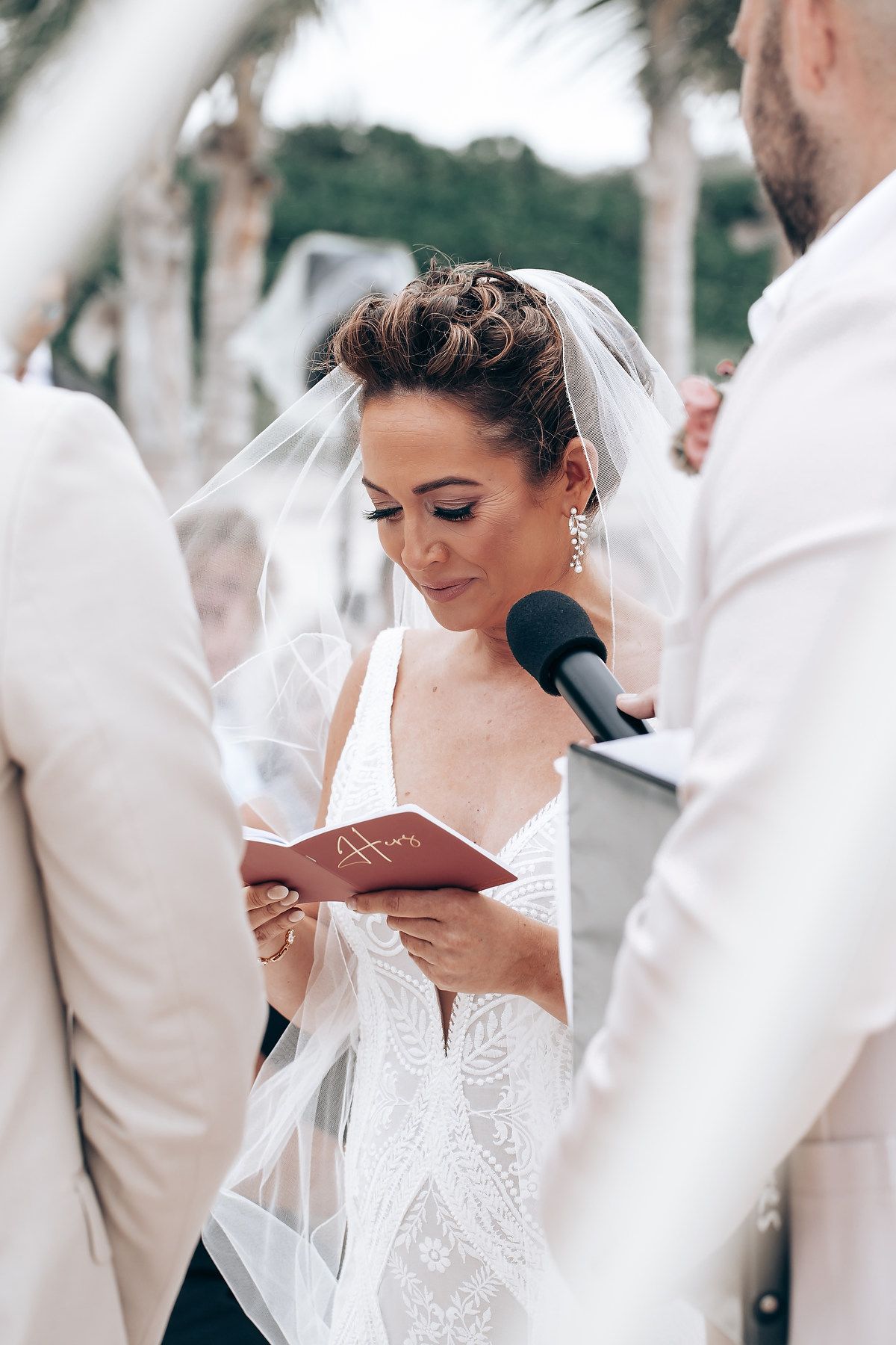 Wedding ceremony moment captured under palm trees with white and beige color scheme.