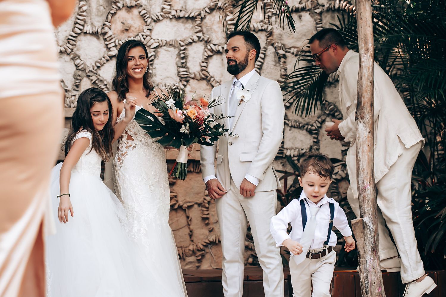 Wedding party celebrates together in an elegant outdoor garden setting with stone walls and tropical foliage.