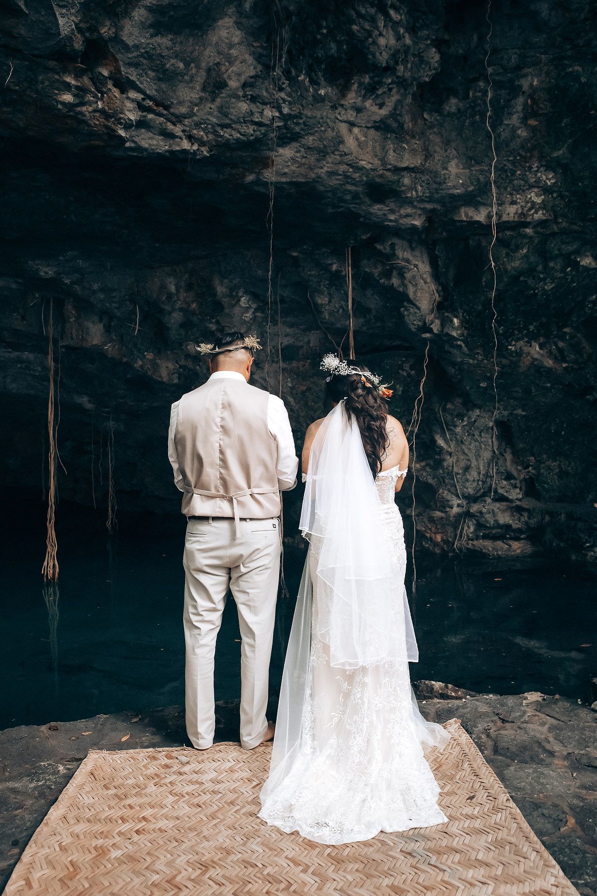 Couple stands on woven mat inside dramatic cave setting for wedding photos.