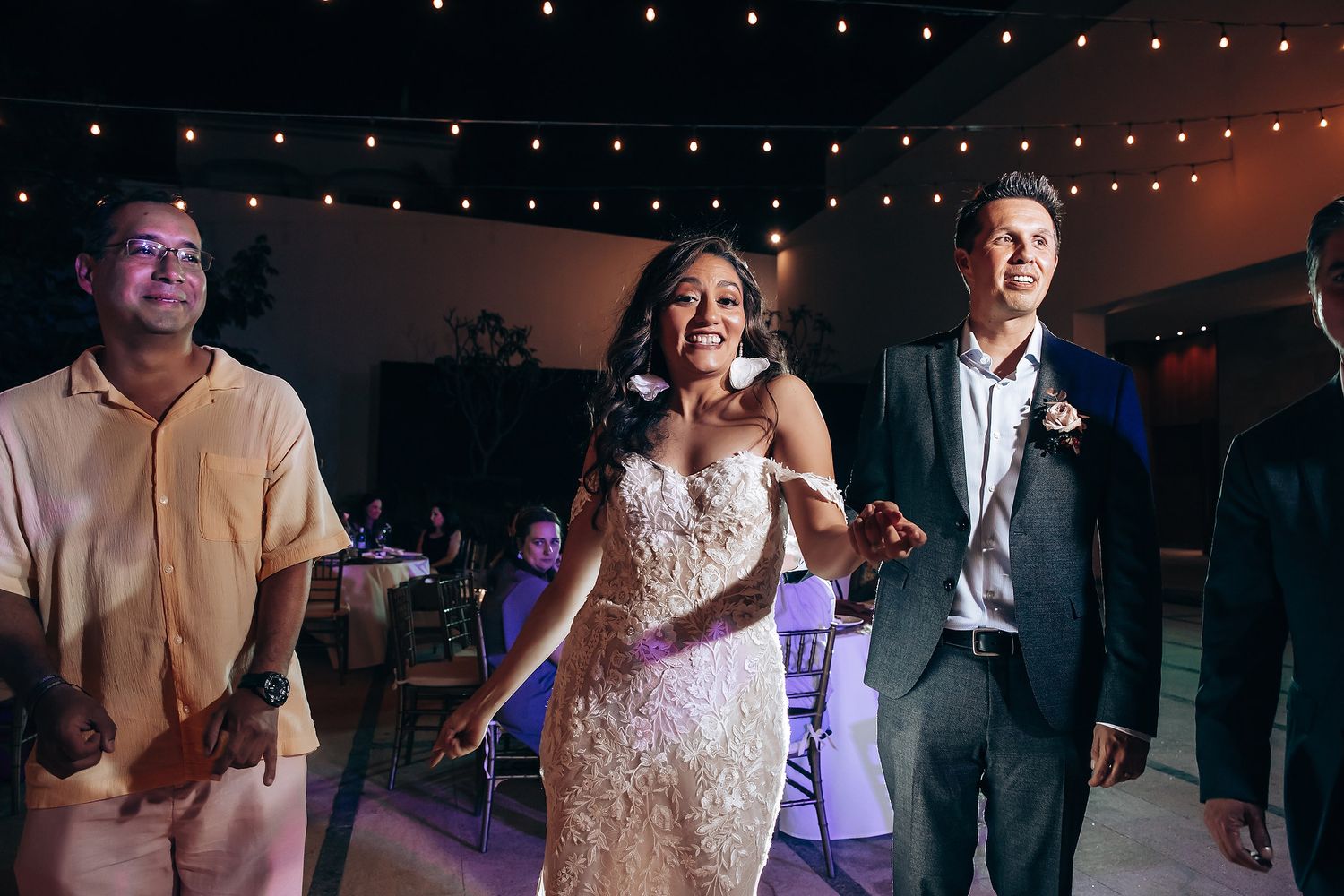 Wedding celebration with guests dancing under twinkling string lights at night.