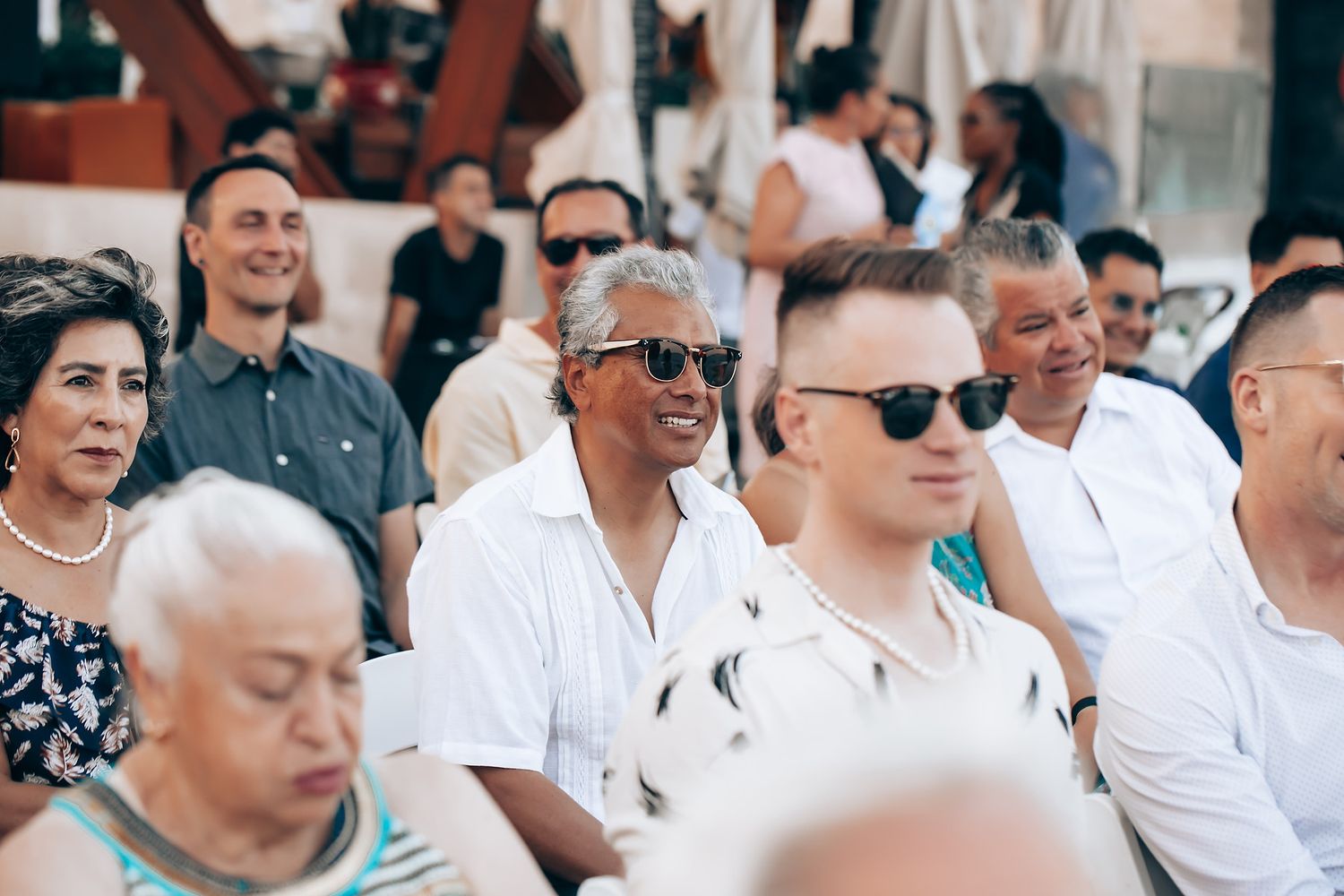 Wedding guests seated outdoors in white attire during ceremony.