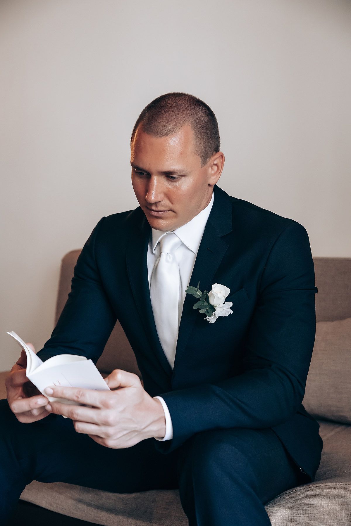 Person in black suit reading letter while seated on couch during wedding preparations.