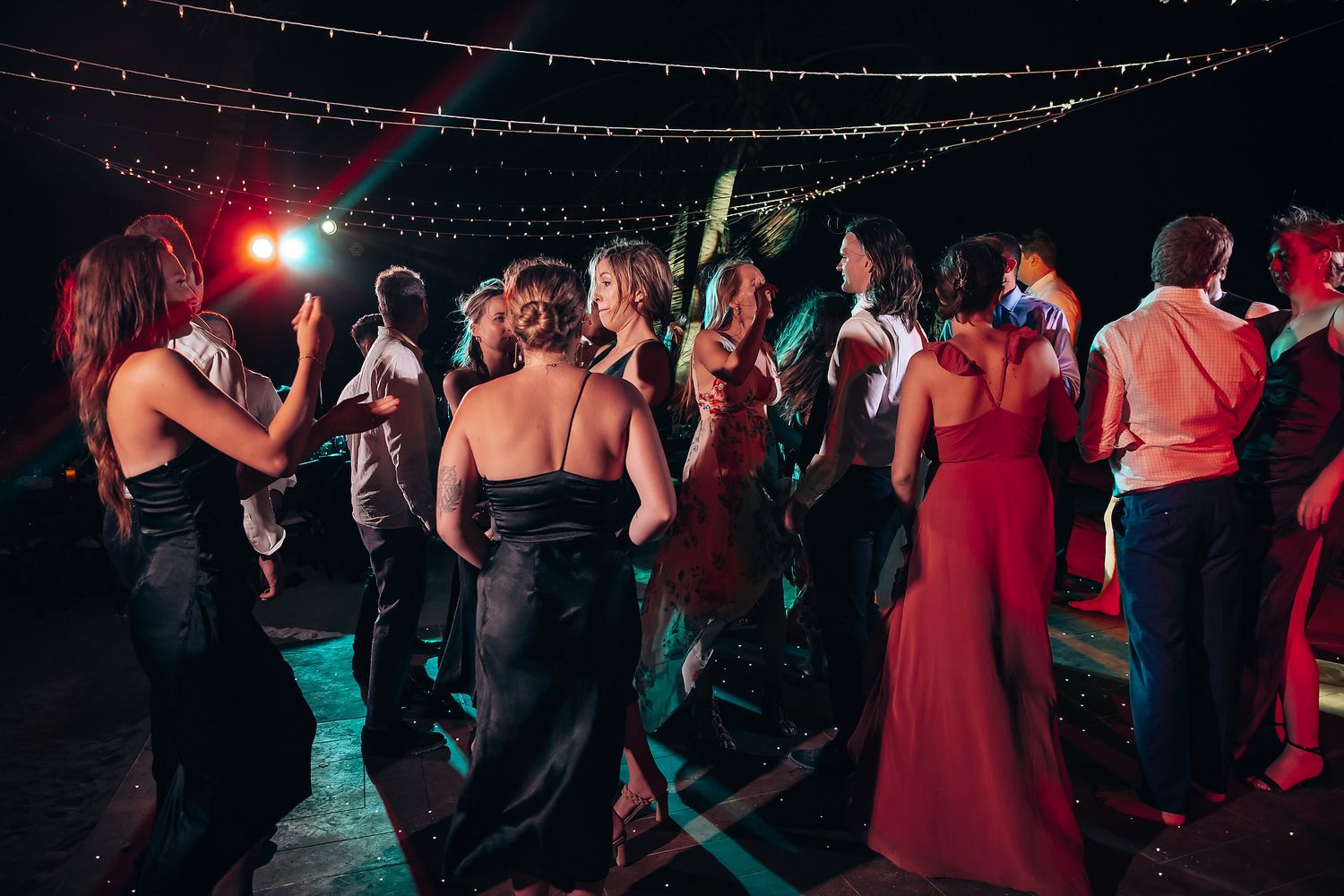 Wedding reception dance floor filled with guests under colorful lighting.