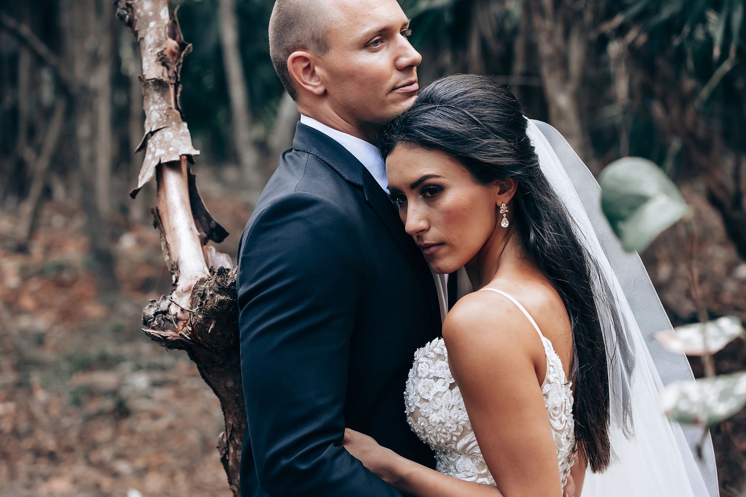 Romantic wedding couple embraces in a wooded area with white tree trunks creating a natural backdrop.