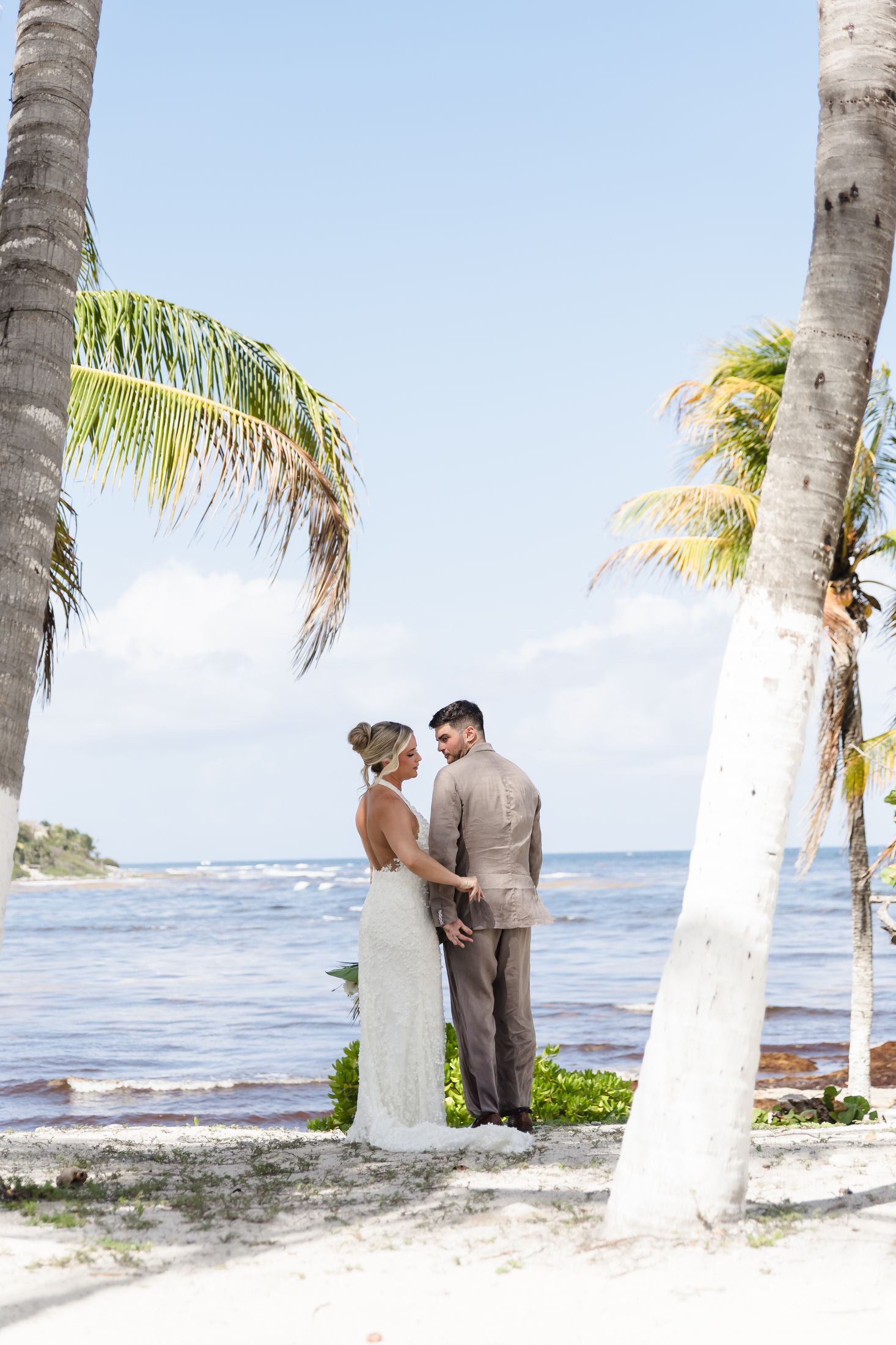 Bride and groom holding hands on tropical beach with palm trees and ocean backdrop on their wedding day.