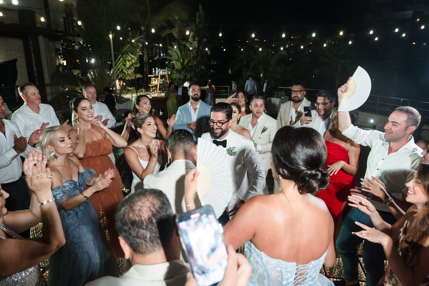 Wedding reception dance floor celebration with bride, groom, and guests cheering outdoors at night.