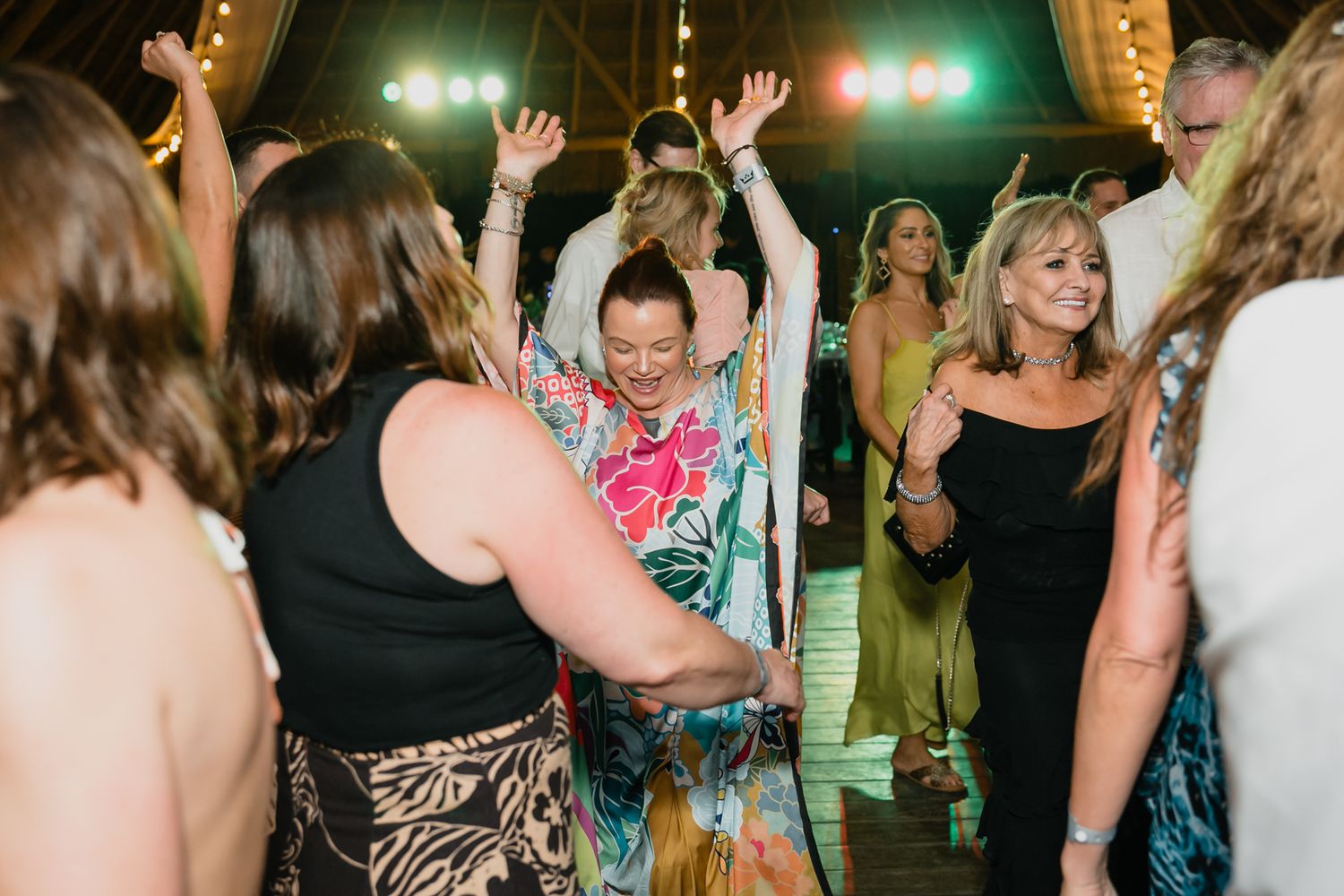 Wedding guests dancing and celebrating with hands raised at a lively tropical reception.