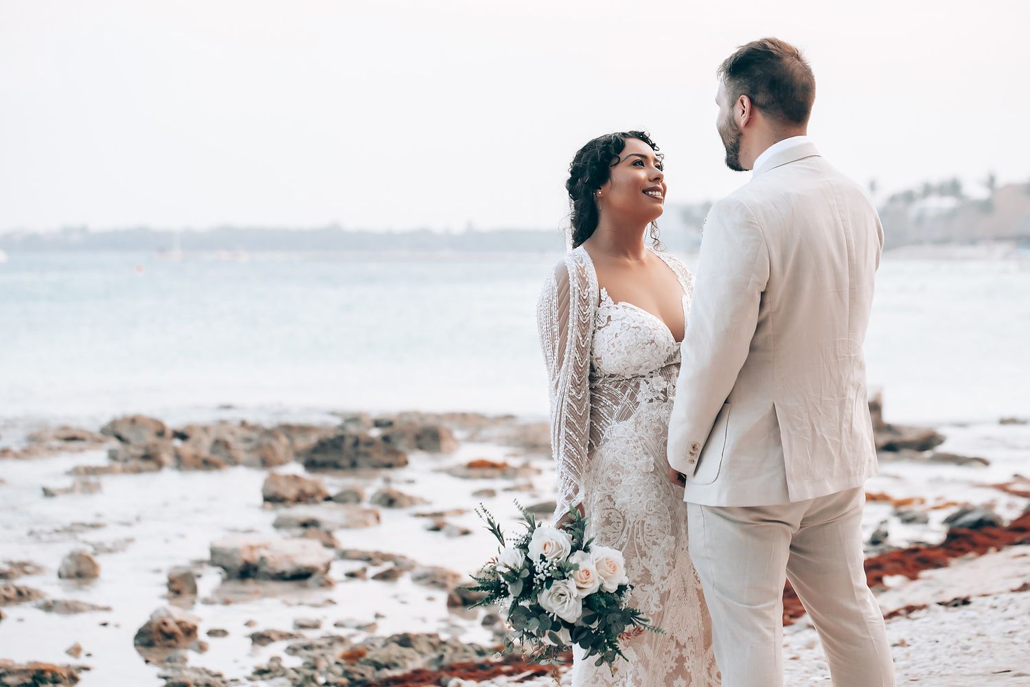 Romantic beach wedding portraits with elegant white attire against a coastal backdrop.