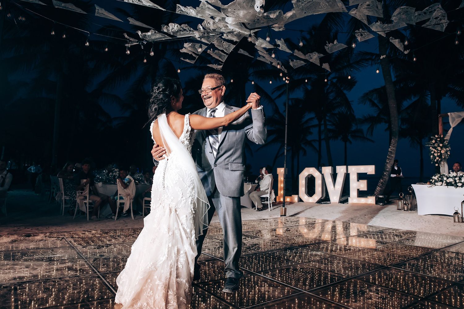A couple shares their first dance at a wedding reception with illuminated LOVE letters in the background.
