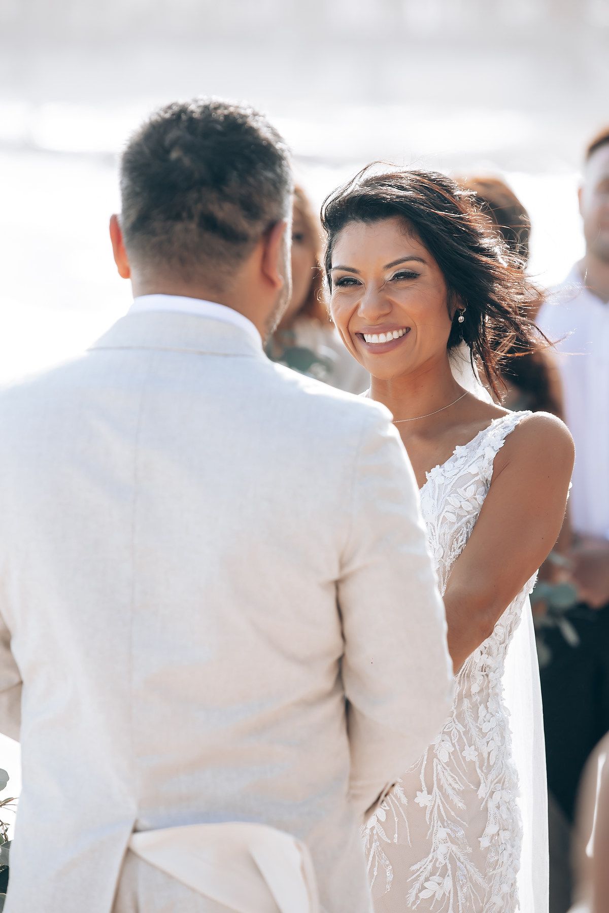 Wedding celebration on a sunny beach with attendees dressed in white enjoying the oceanfront atmosphere.