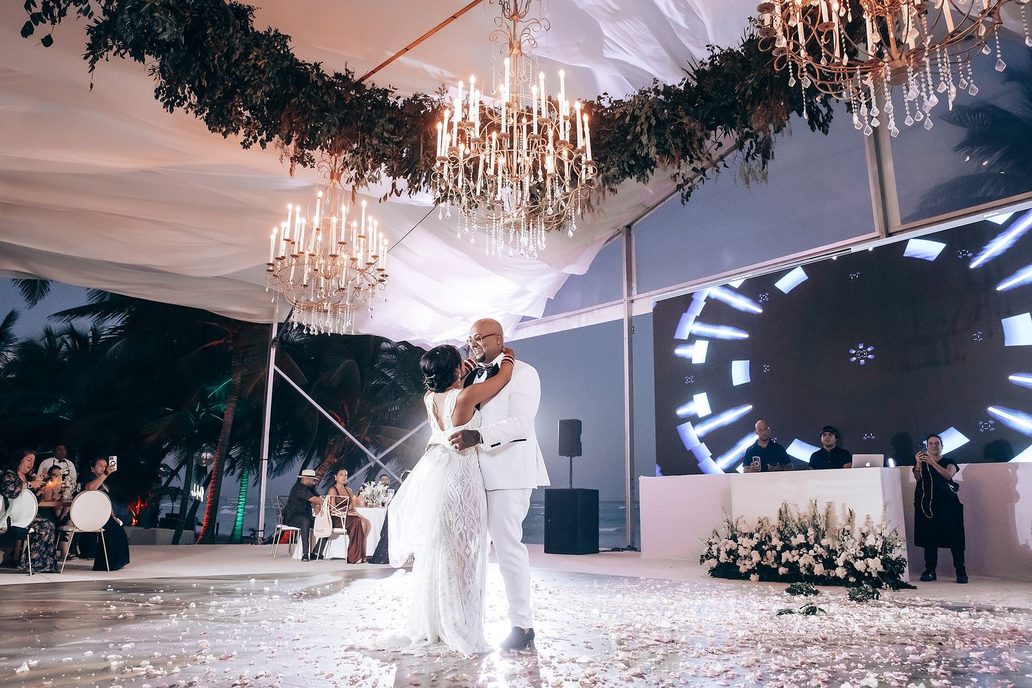 Wedding reception tent illuminated by chandeliers as guests celebrate on the dance floor.