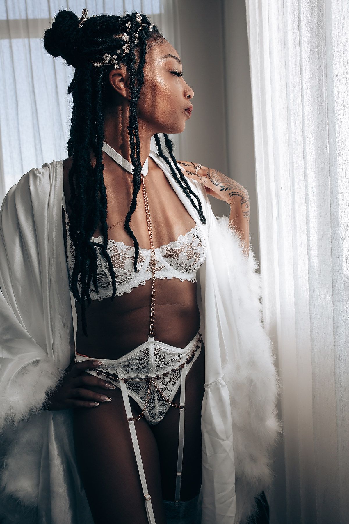 Artistic boudoir photo featuring braided hair with floral accessories and white silk robe.