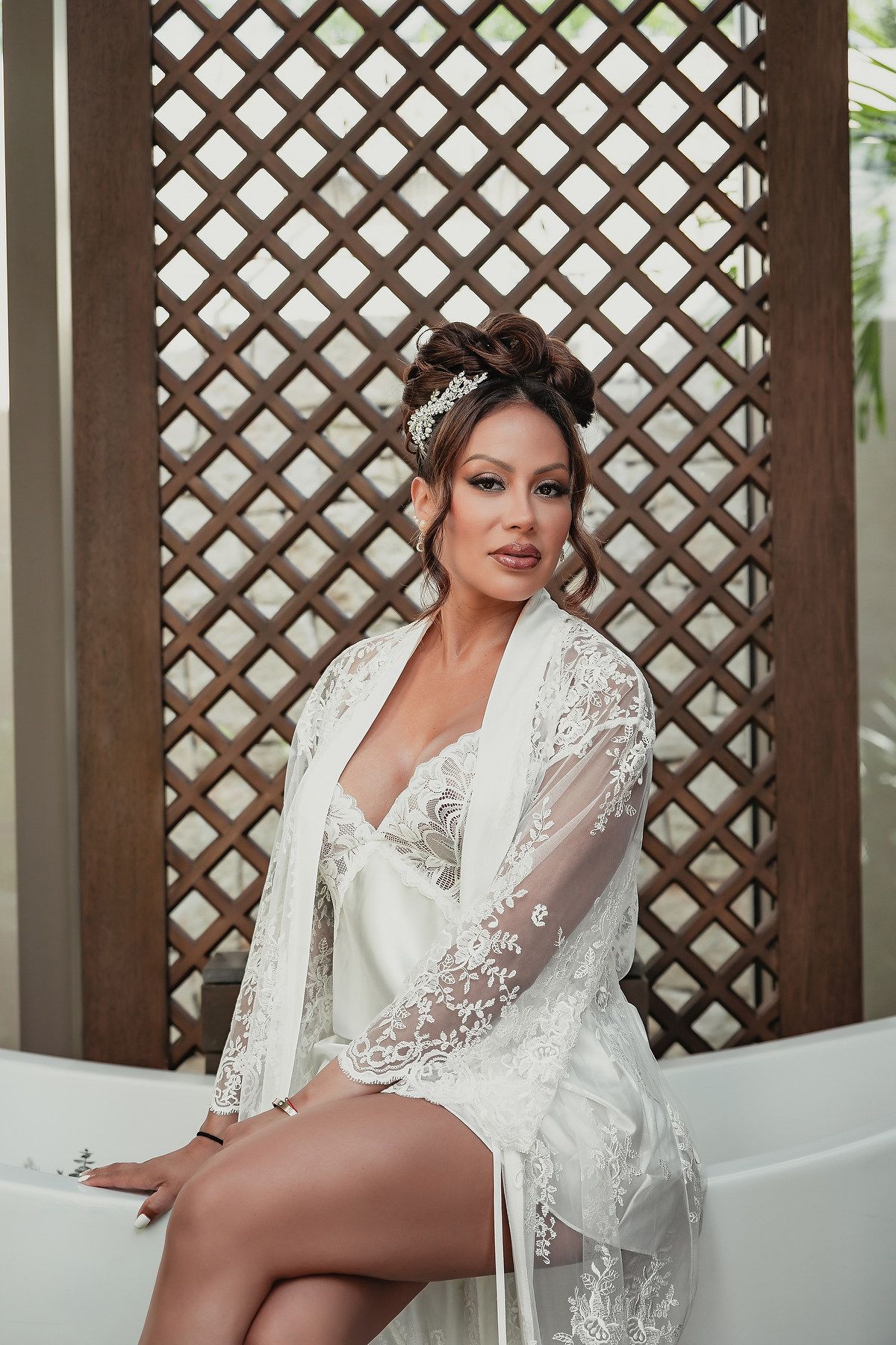 Bridal boudoir photo session featuring white lace robe in an elegant setting with lattice backdrop.