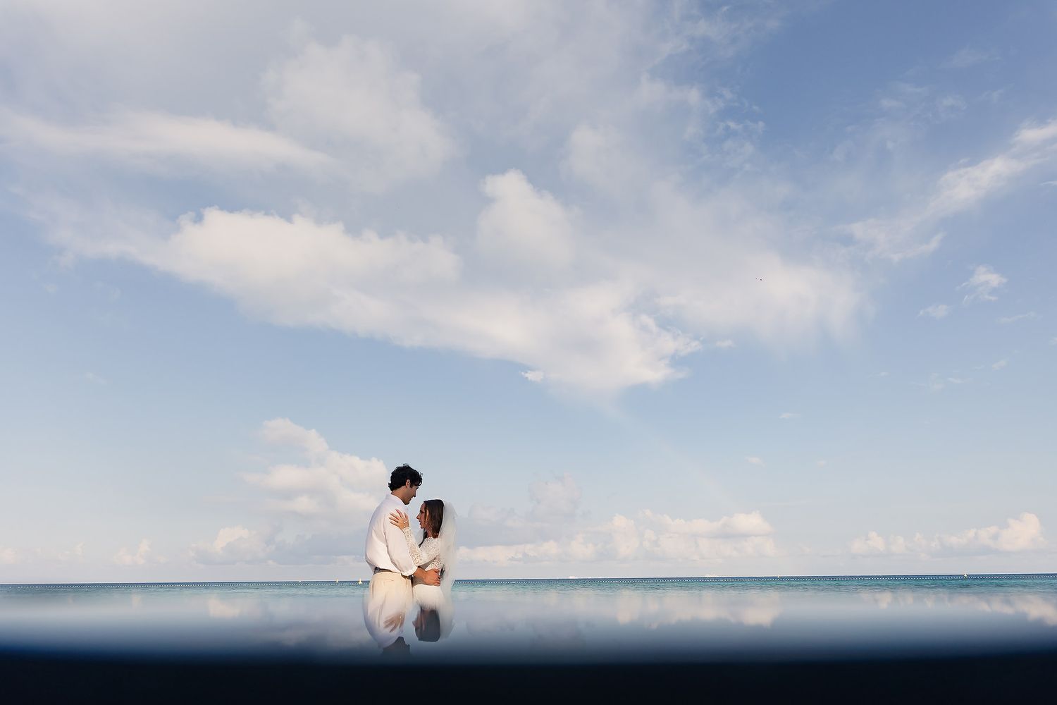 Romantic oceanfront wedding photo against blue sky and horizon.