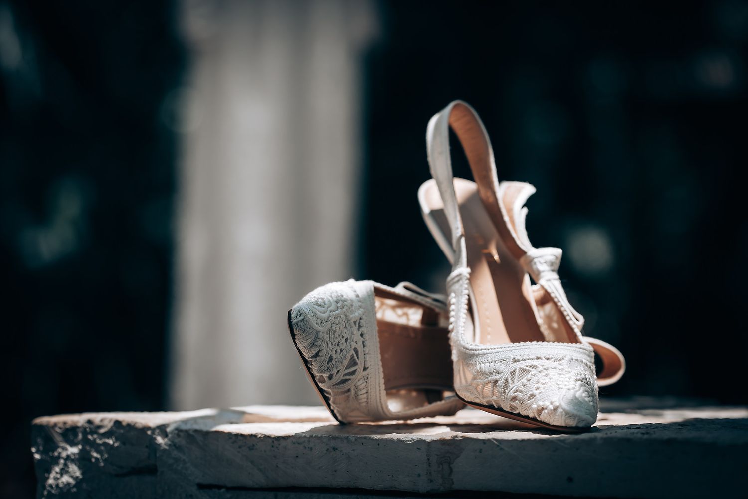 A collection of elegant white bridal shoes arranged on a dark surface in a studio setting.