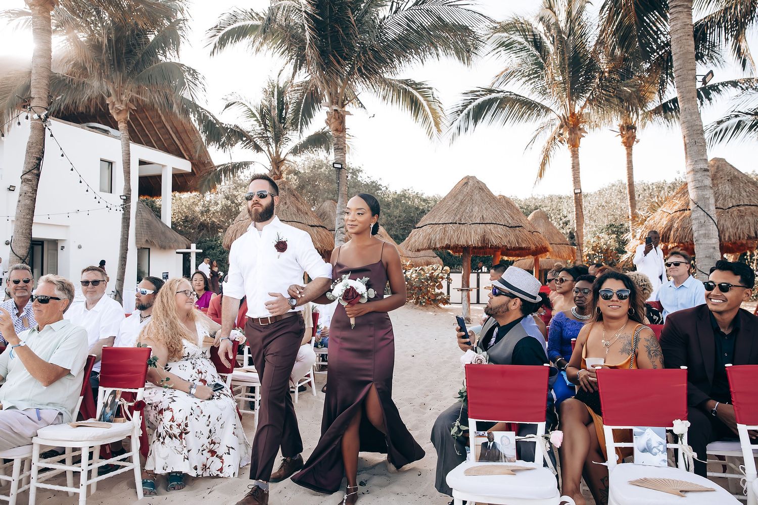 Beachfront wedding ceremony setup with white chairs and tropical decor under swaying palm trees.