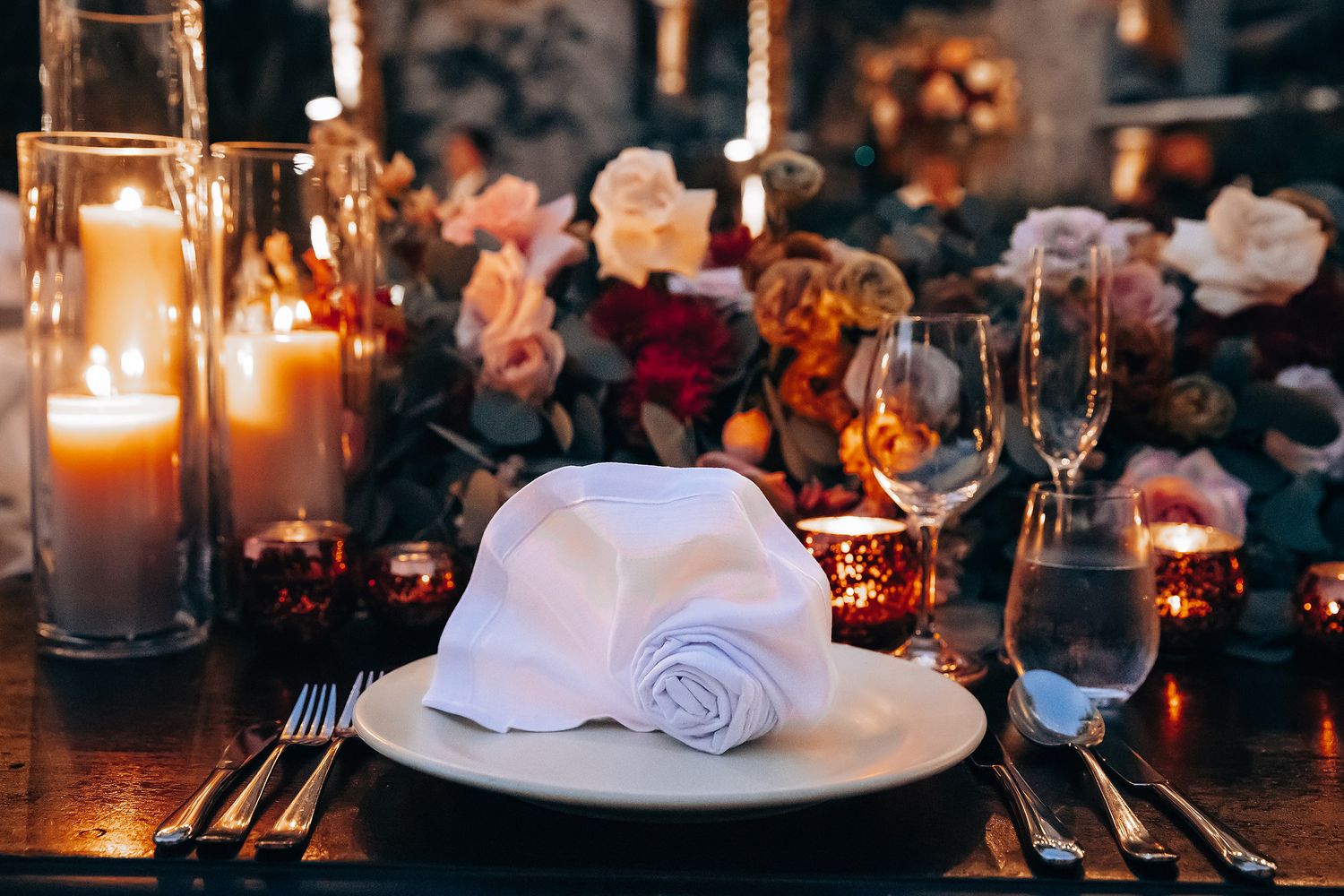 Elegant wedding reception table setting with glowing candles and formal place settings.