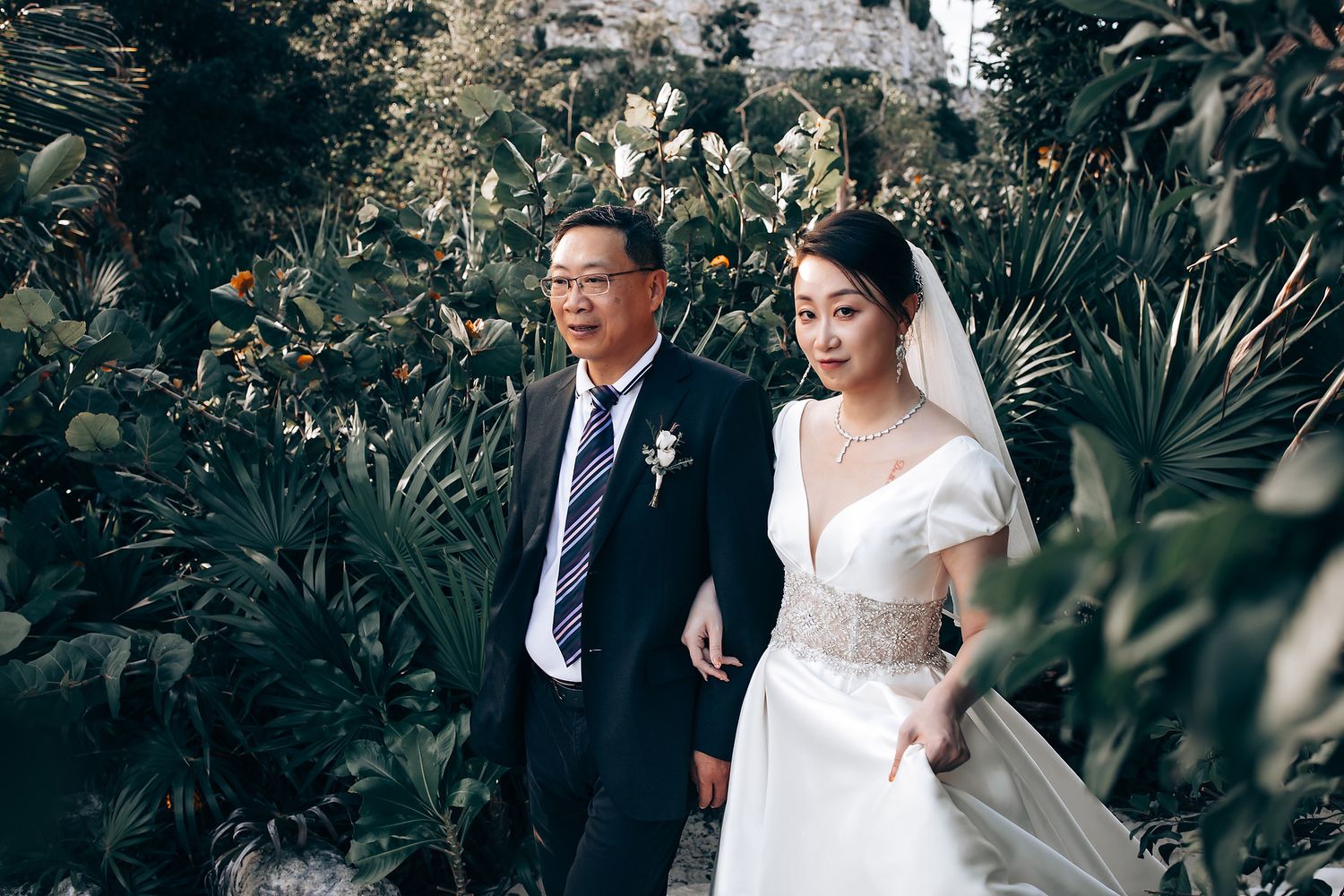 Elegant wedding couple walking through a lush garden pathway.