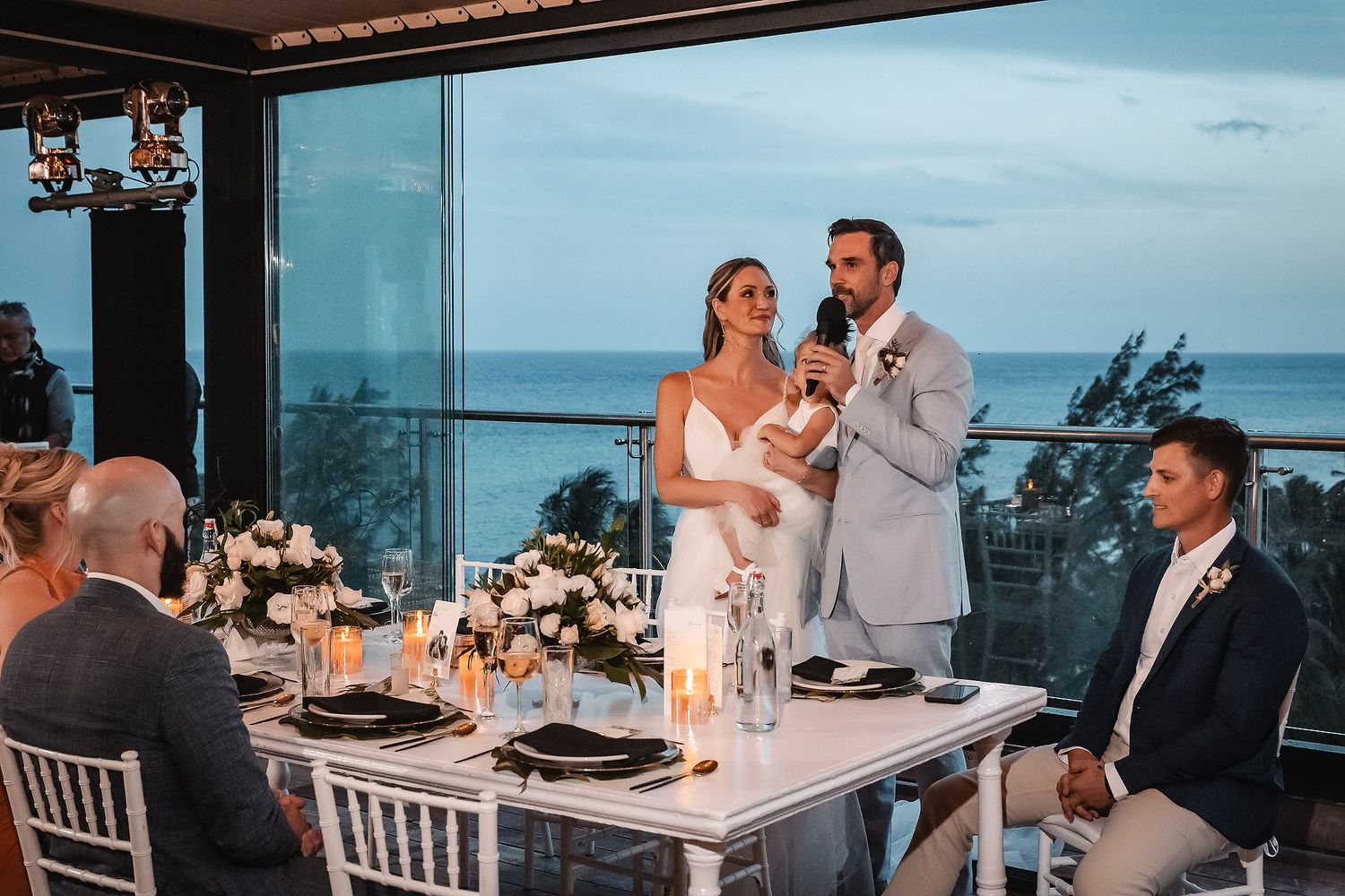 Wedding reception dinner setup with ocean view backdrop and elegant table settings.