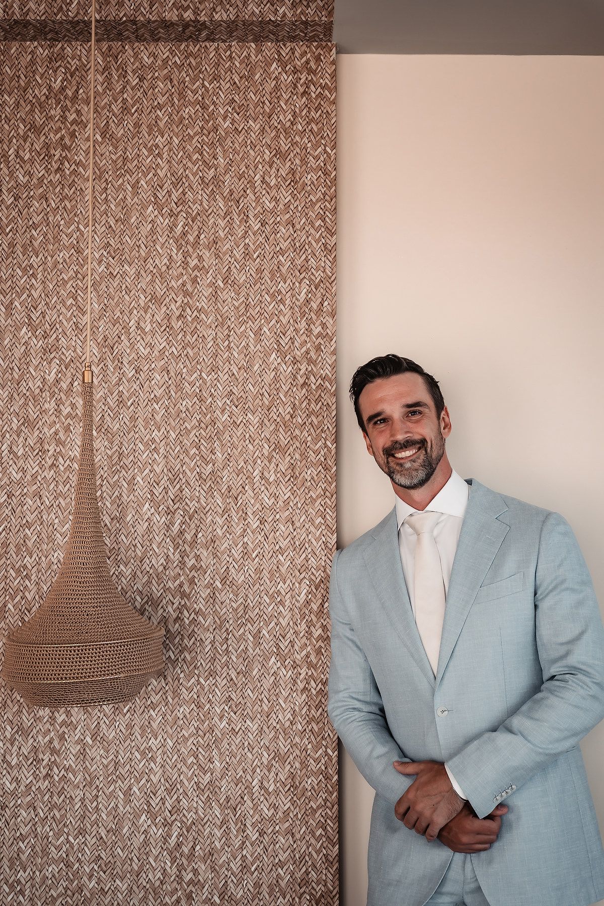 Person in light blue suit smiling against textured wallpaper background.