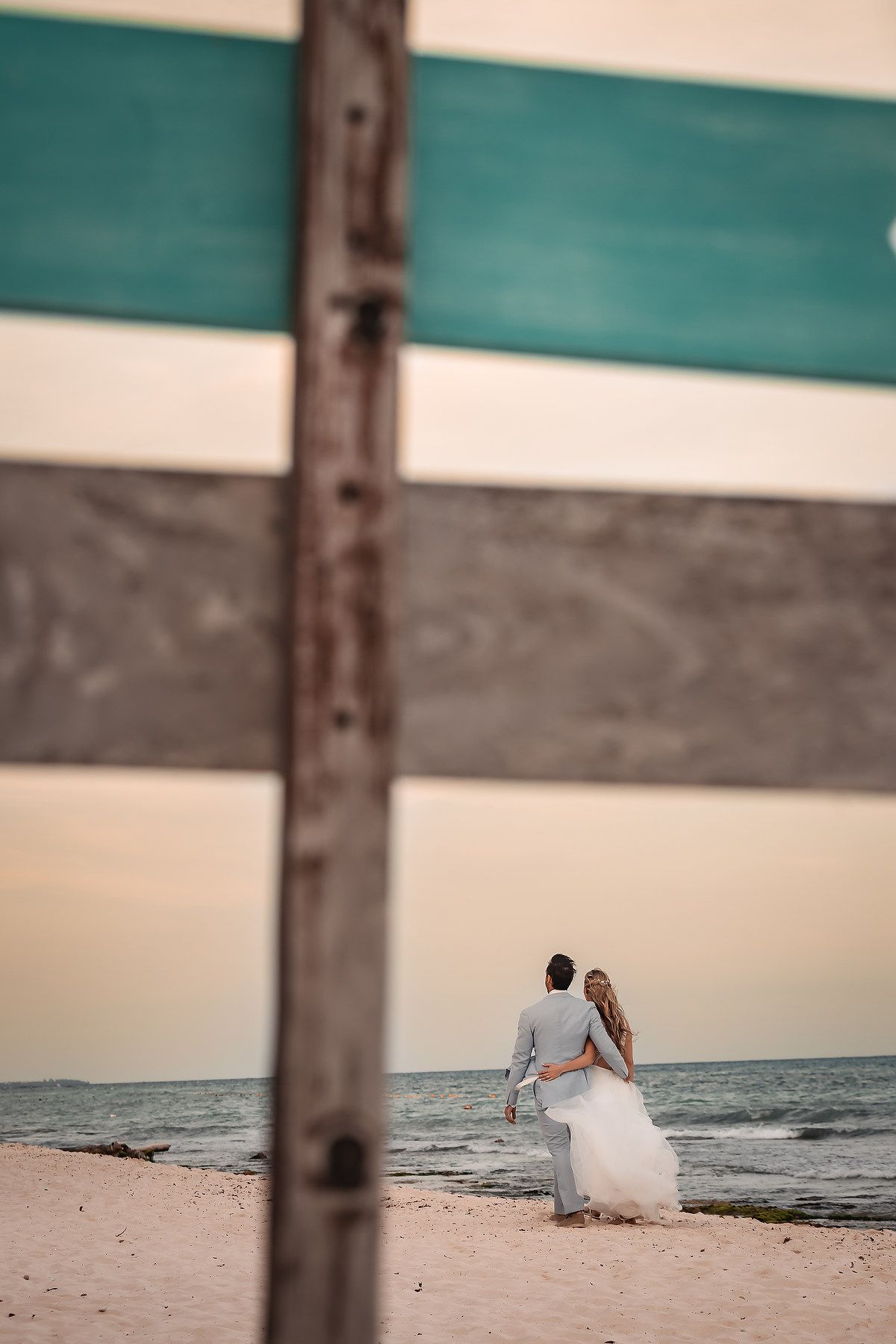 Beach wedding photography through wooden fence posts at sunset.