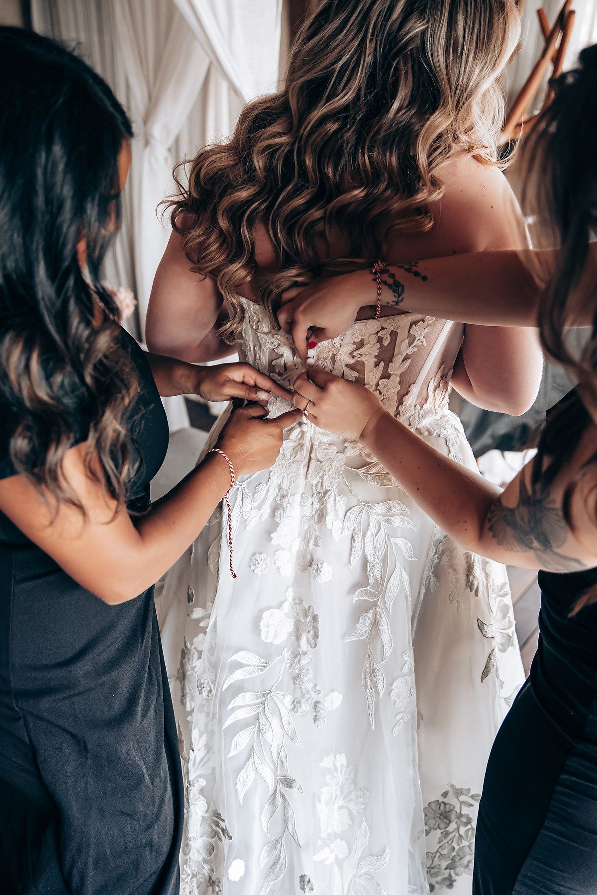 Close-up shots of helping hands lacing up a detailed white wedding dress.