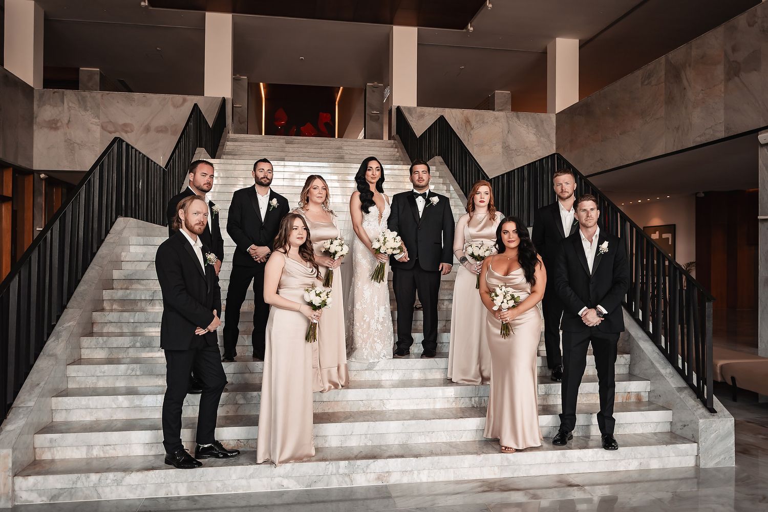 Wedding party poses elegantly on grand stone staircase in formal attire.