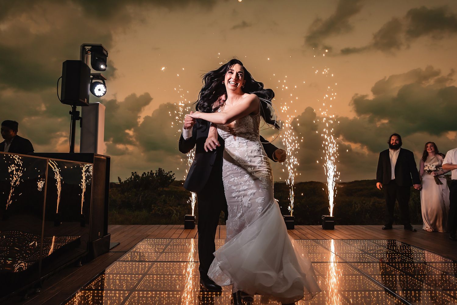 Dramatic nighttime wedding celebration with sparklers and fireworks against a dusky sky.