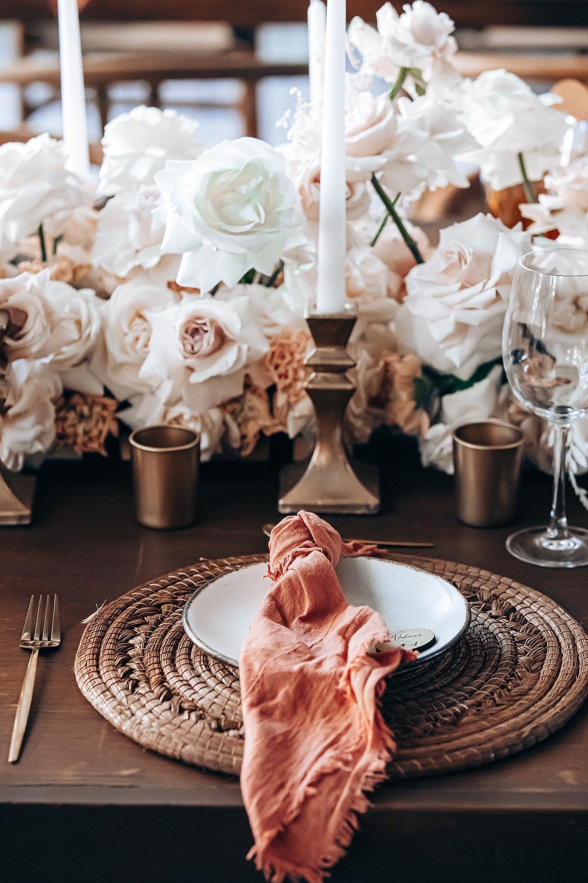 Elegant table setting with white flowers and coral napkins on woven placemats for a romantic dinner party.