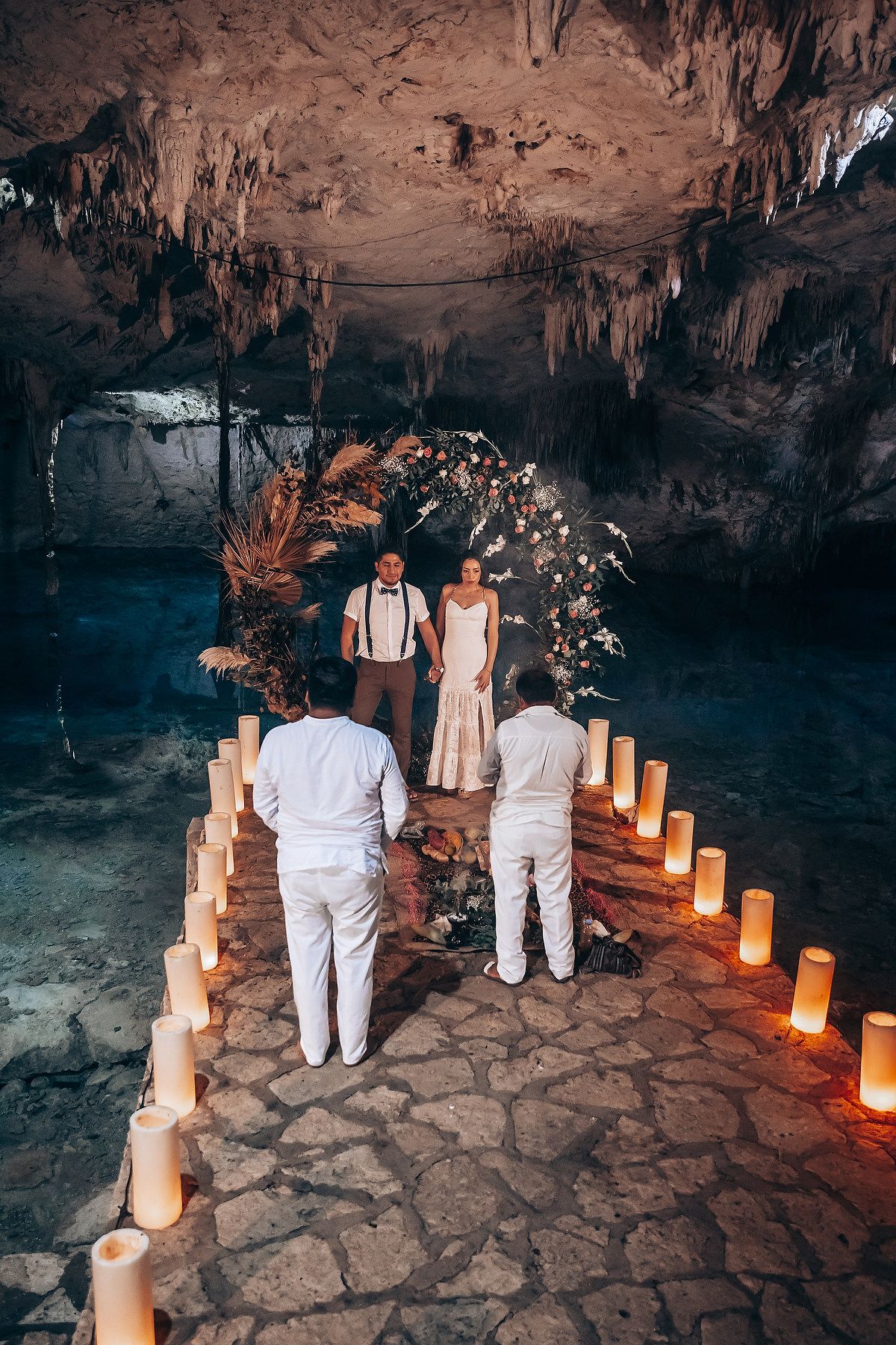 A romantic cave wedding ceremony setup with glowing candles lining a stone path and natural rock formations overhead.