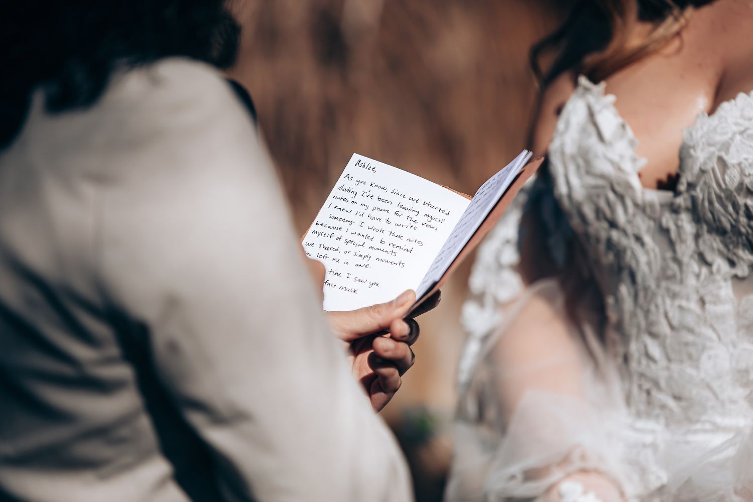 Person writing in a notebook with a pen while holding a smartphone in natural lighting.