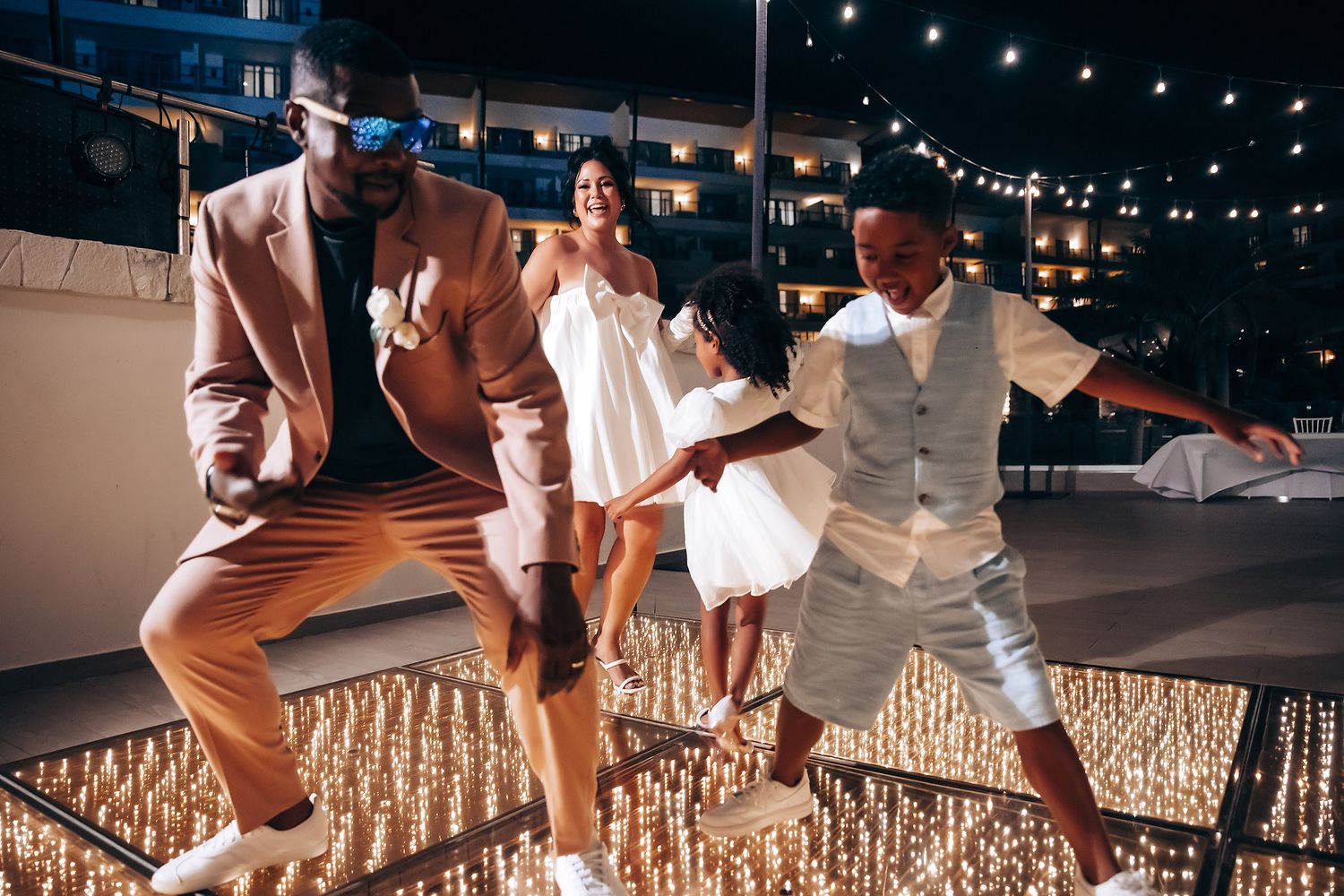 Wedding guests dance joyfully on an outdoor dance floor under string lights at a reception celebration.