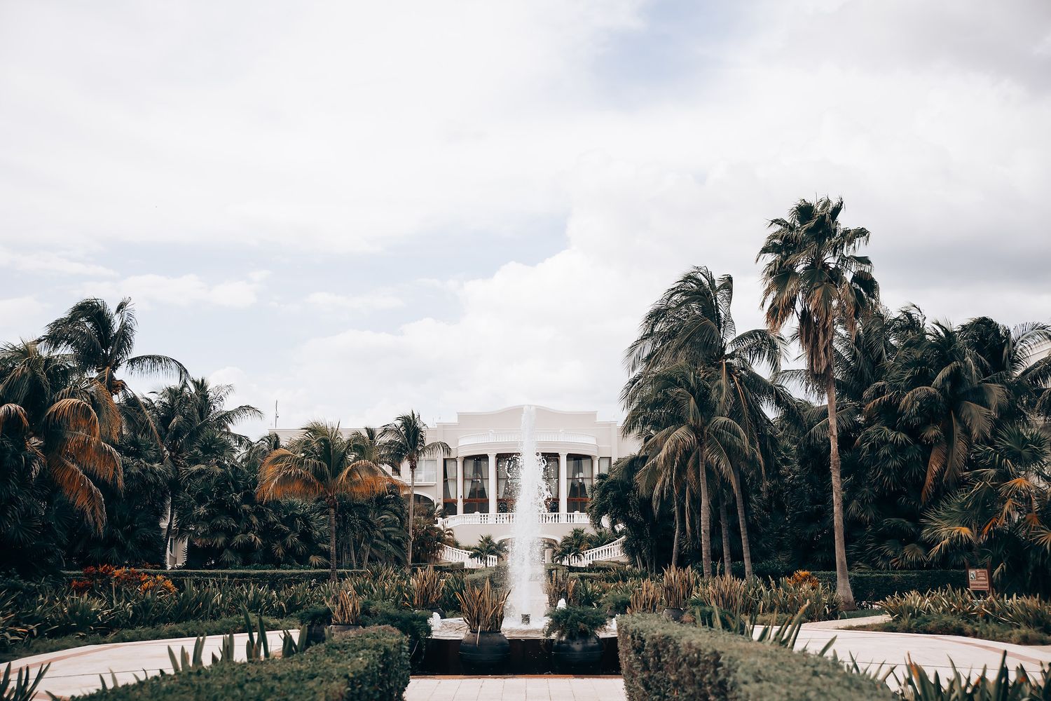 A panoramic view of a coastal resort property with swaying palm trees and white buildings against a cloudy sky.