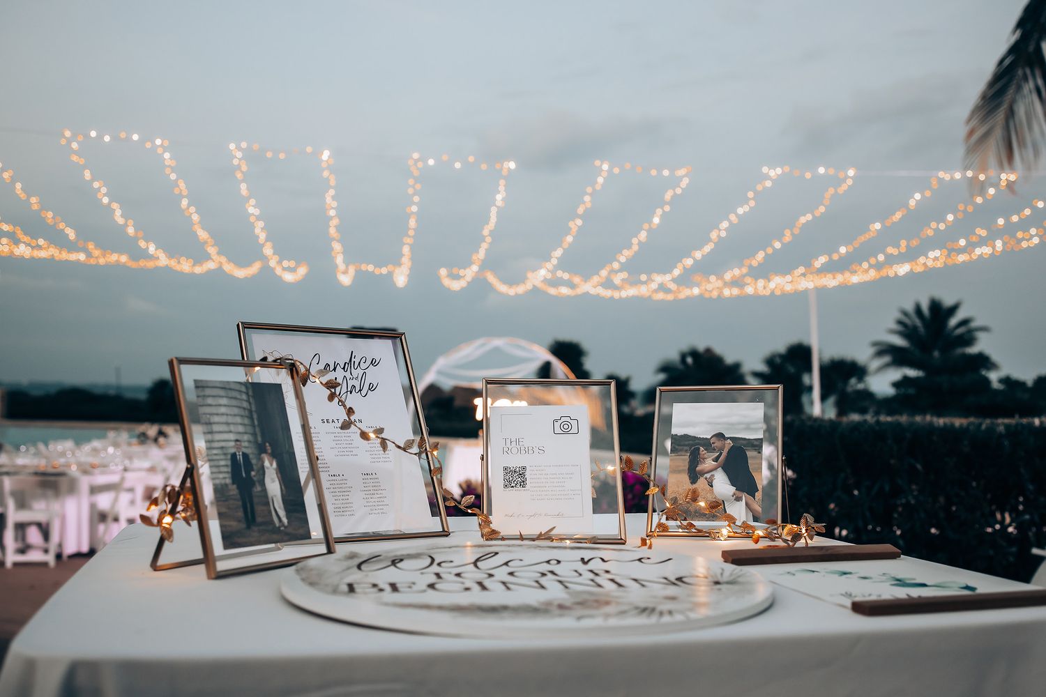 Wedding reception setup with string lights and white decor elements at dusk.