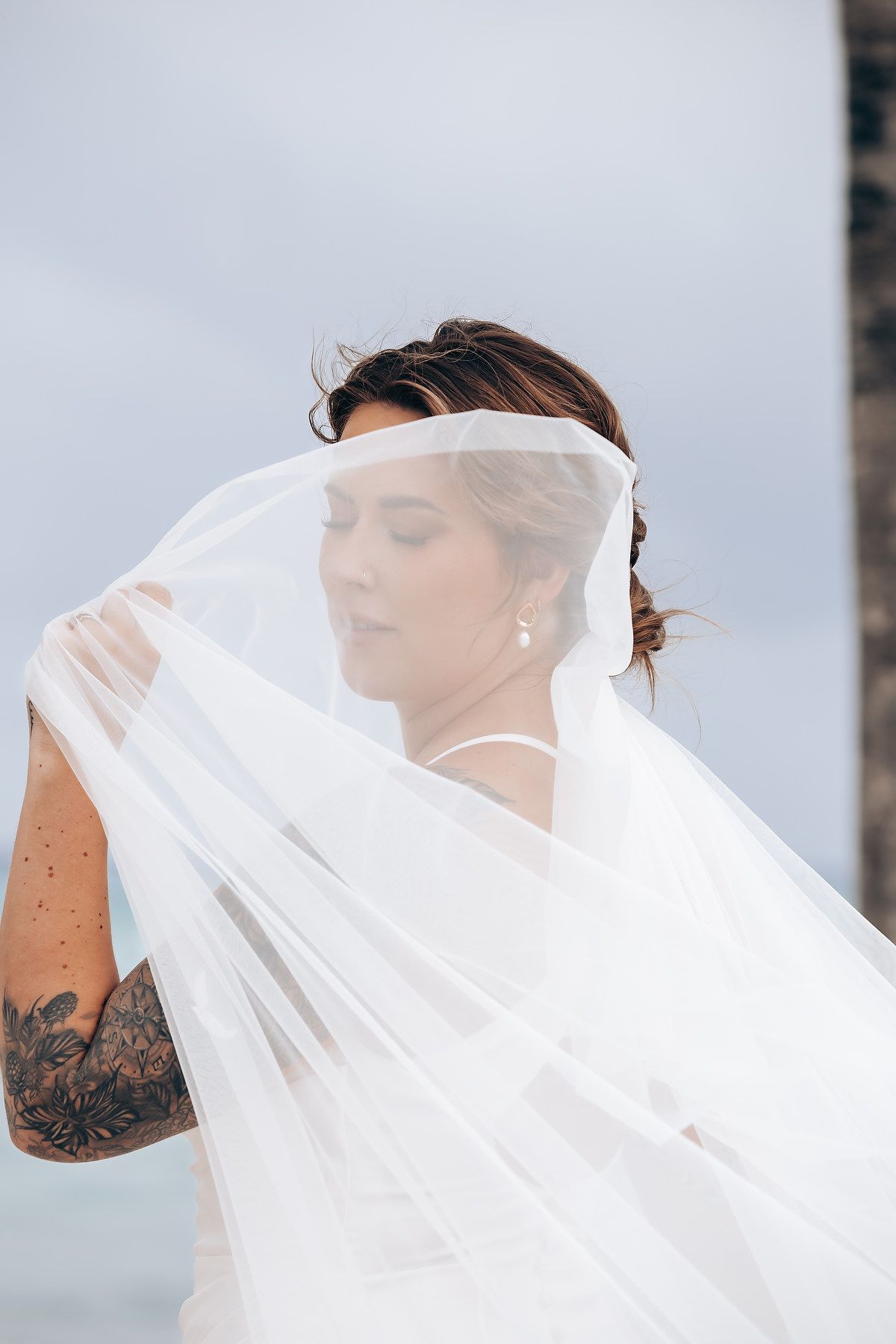 Flowing white wedding veil catches the breeze against a soft cloudy background.
