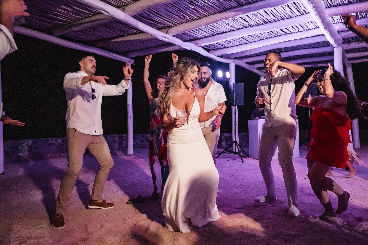 Wedding reception dance party under purple lighting with guests celebrating.